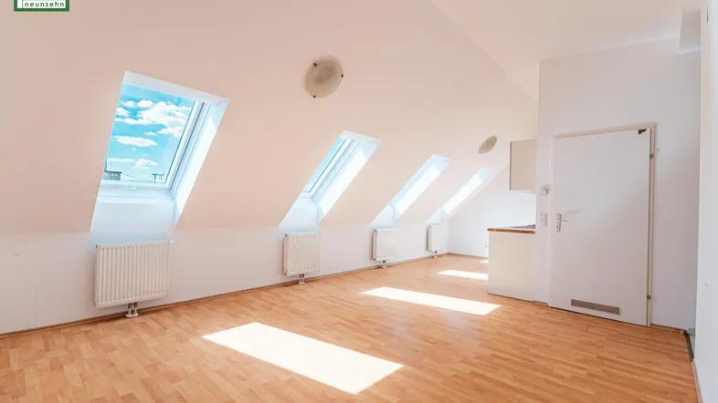Heller Wohnbereich im Dachgeschoss mit Holzboden, Dachfenstern und integrierter Küchenzeile.