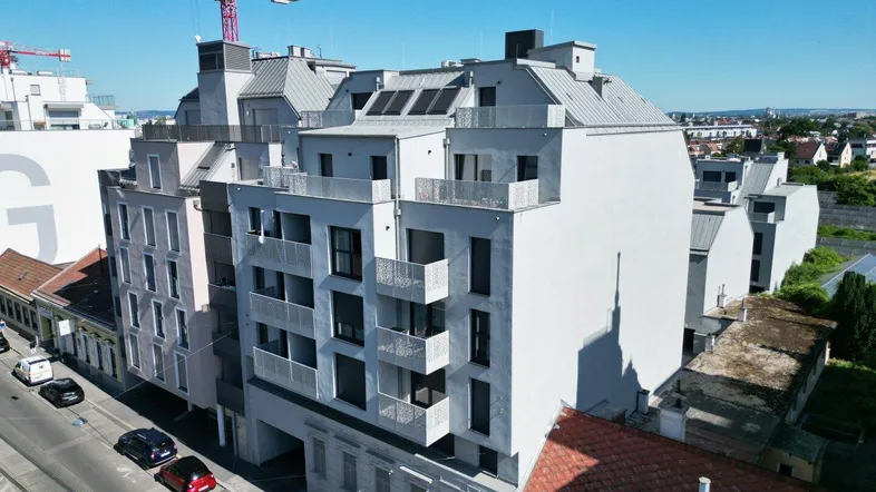 Moderne Wohngebäude-Fassade mit Balkonen und Dachterrassen in städtischer Umgebung, teilweise noch im Bau.