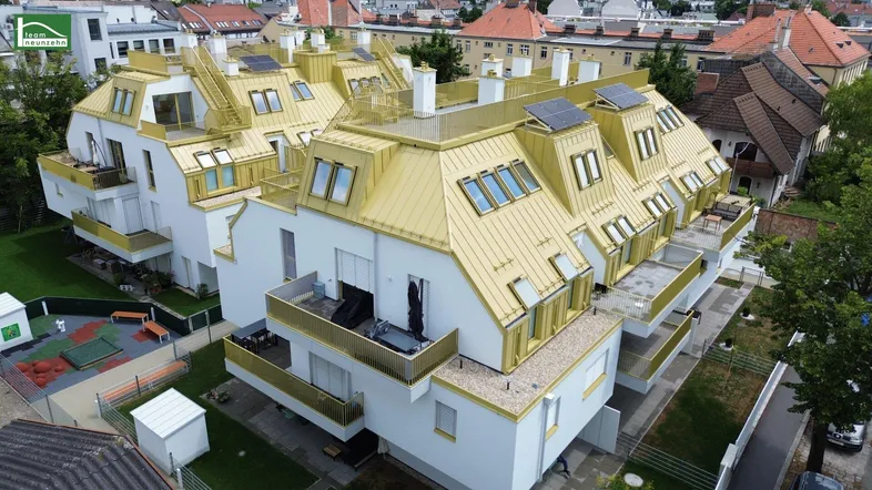 Luftaufnahme eines modernen Wohnkomplexes mit goldfarbenen Dächern, Solarpaneelen und einem Spielplatz.