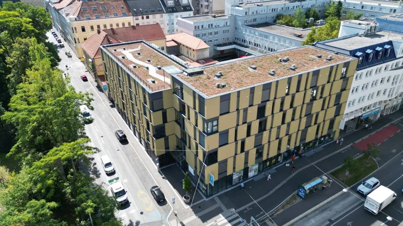 Luftaufnahme eines modernen Gebäudes mit begrüntem Flachdach in städtischer Umgebung.