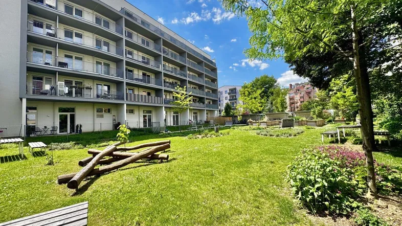 Moderner Wohnbau mit Balkonen und einem gepflegten Gemeinschaftsgarten mit Sitzgelegenheiten und Grünflächen.
