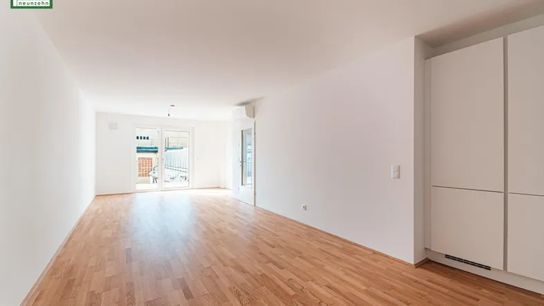 Geräumiger, leerer Wohn-Essbereich mit hellem Holzboden und Zugang zu einem Außenbereich.