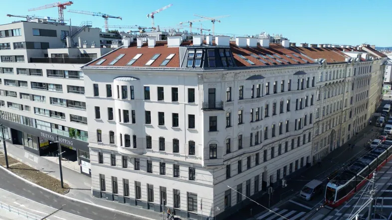 Luftaufnahme eines Altbaus mit Mansarddach und umliegender Stadtlandschaft mit Baustellenkränen.