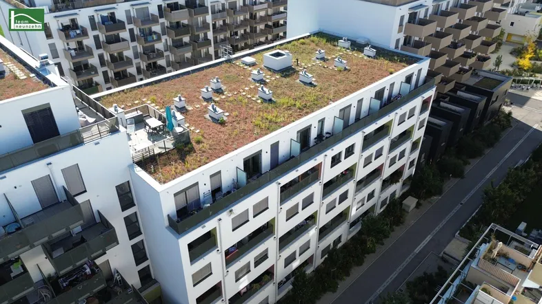 Luftaufnahme eines modernen Wohnkomplexes mit begrünten Dächern und Balkonen in einer städtischen Umgebung.
