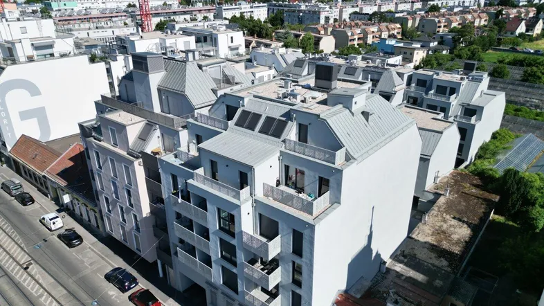 Luftaufnahme eines modernen Wohnkomplexes in städtischer Umgebung mit umliegenden Gebäuden und Dächern.