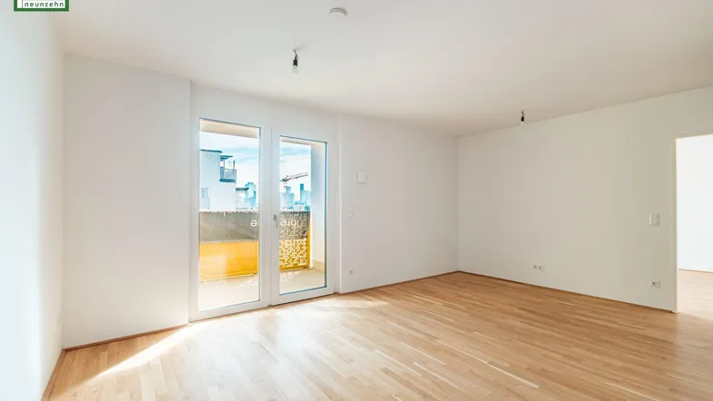 Helles, leeres Wohnzimmer mit Parkettboden und direktem Zugang zum Balkon.