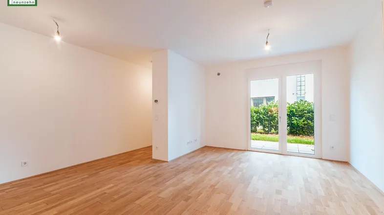 Helles, leeres Wohnzimmer mit Parkettboden und Zugang zu einem kleinen Außenbereich.