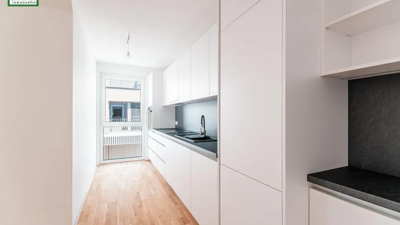 Moderne, helle Küche mit weißen Schränken, dunkler Arbeitsplatte und Zugang zum Balkon.