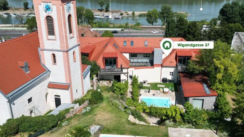 Luftaufnahme des Anwesens mit Kirche, zwei Pools und Blick auf den Kuchelauer Hafen und die Donau.