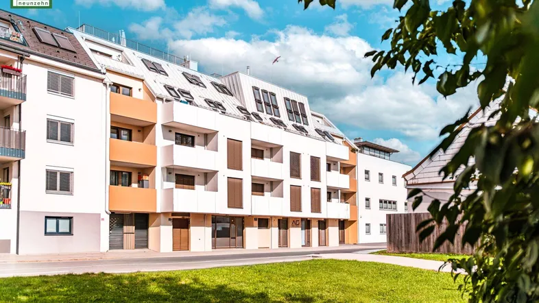 Moderne Wohnanlage mit weißer Fassade, Balkonen und grüner Umgebung unter blauem Himmel.
