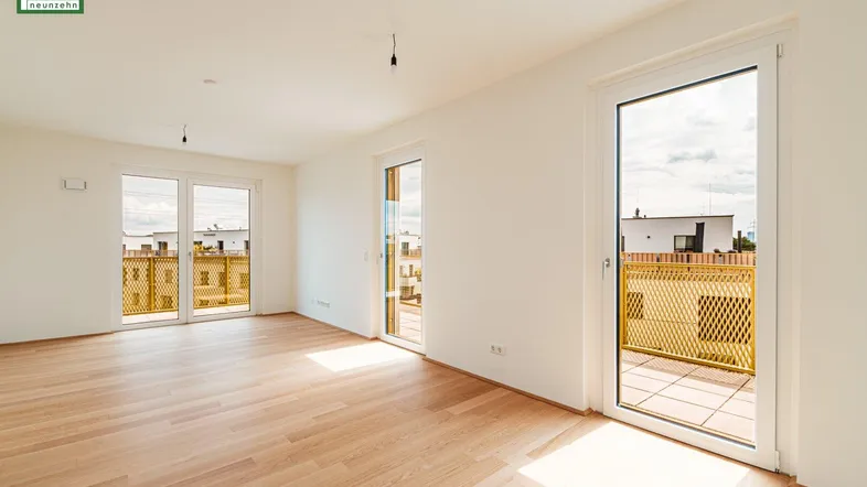 Geräumiges Wohnzimmer mit Parkettboden und mehreren Balkontüren, die viel Licht hereinlassen.