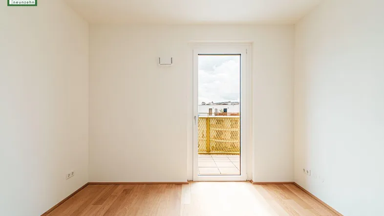 Heller Raum mit Holzboden und Zugang zu einem Balkon oder einer Terrasse.