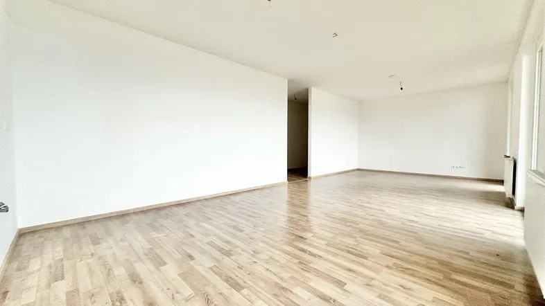 Geräumiger, leerer Wohnbereich mit hellem Holzboden und weißen Wänden, bereit zur Einrichtung.