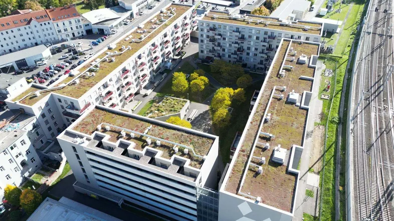 Luftaufnahme von modernen Wohngebäuden mit begrünten Flachdächern und einem gepflegten Innenhof in städtischer Umgebung.