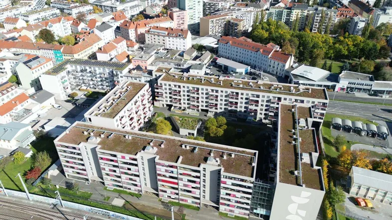 Luftaufnahme eines großen Wohnkomplexes mit begrünten Dächern und Innenhof in städtischer Umgebung.