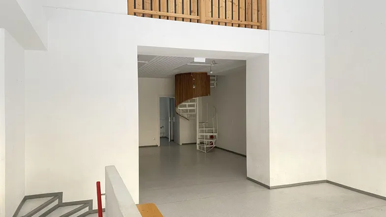 Geräumiger, leerer Gewerberaum mit hoher Decke, Wendeltreppe und Holzgeländer zur Empore.