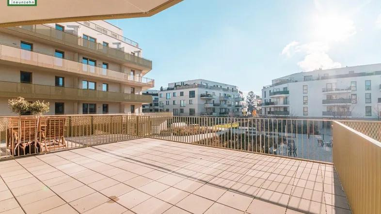 Große, sonnige Terrasse mit Fliesenboden und Blick auf die umliegenden modernen Gebäude.