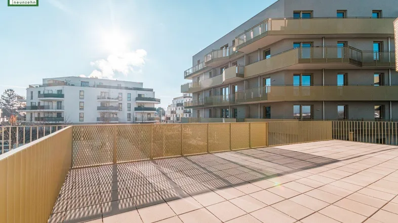 Weitläufige Sonnenterrasse mit Fliesenboden und Blick auf die umliegenden modernen Gebäude.