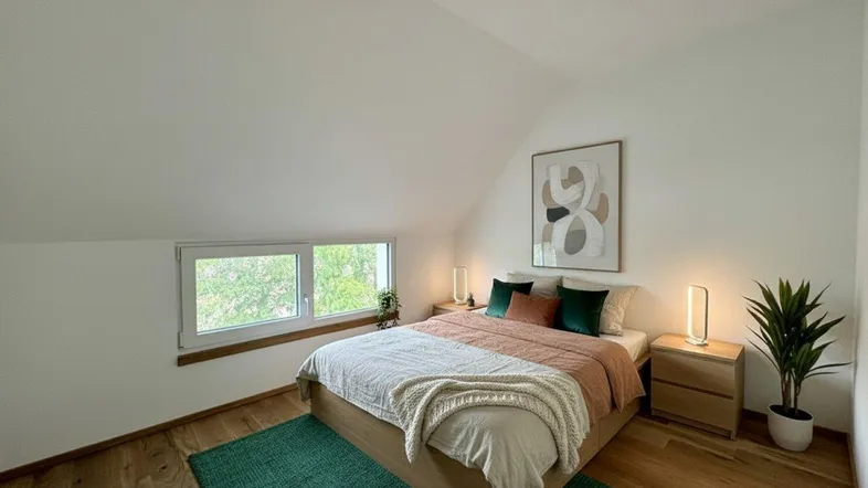 Gemütliches Schlafzimmer im Dachgeschoss mit Holzboden, schräger Decke und Blick ins Grüne.