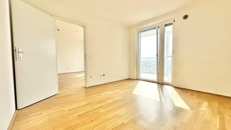 Helles, leeres Zimmer mit Holzboden und Zugang zu einem Balkon, bereit zur individuellen Gestaltung.