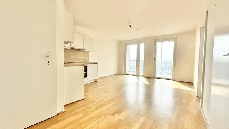 Heller Wohnbereich mit offener Küchenzeile, Parkettboden und Zugang zum Balkon.
