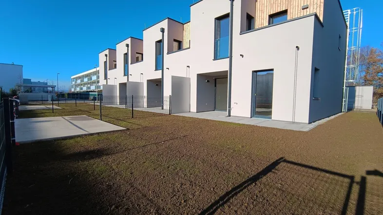 Moderne Reihenhäuser mit heller Fassade und Holzverkleidung, umgeben von noch unfertigen Gärten.