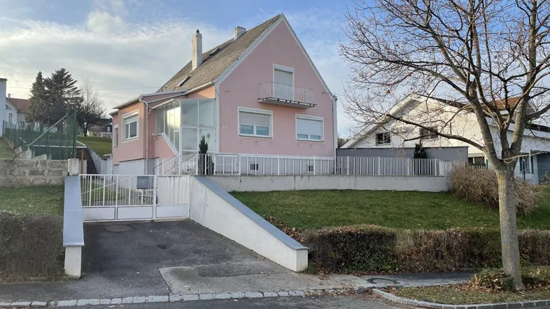 Rosa Einfamilienhaus mit Balkon, Wintergarten und Zufahrt in ländlicher Umgebung.