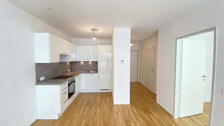 Moderne, offene Küche mit weißen Hochglanzschränken und Holzboden, die in einen Flur übergeht.