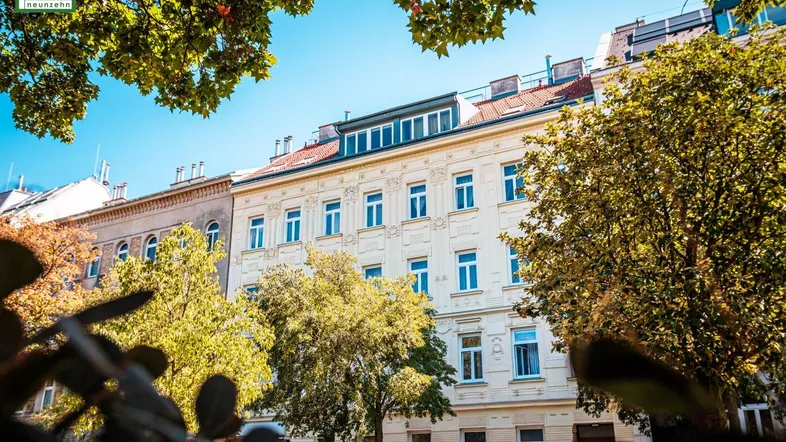 Klassisches Wiener Wohnhaus mit heller Fassade und Dachausbau, umgeben von Bäumen.