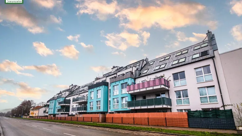 Moderne Wohngebäude mit farbigen Balkonen und Dachfenstern entlang einer Straße unter bewölktem Himmel.
