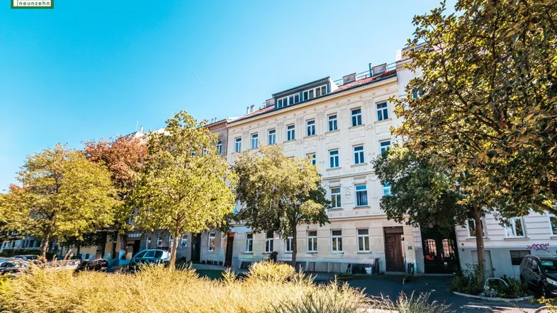 Historisches Wohngebäude mit klassischer Fassade und begrüntem Vorgarten unter blauem Himmel.