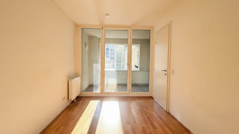 Helles Zimmer mit Parkettboden und großen Glasfronten, die viel Sonnenlicht hereinlassen.