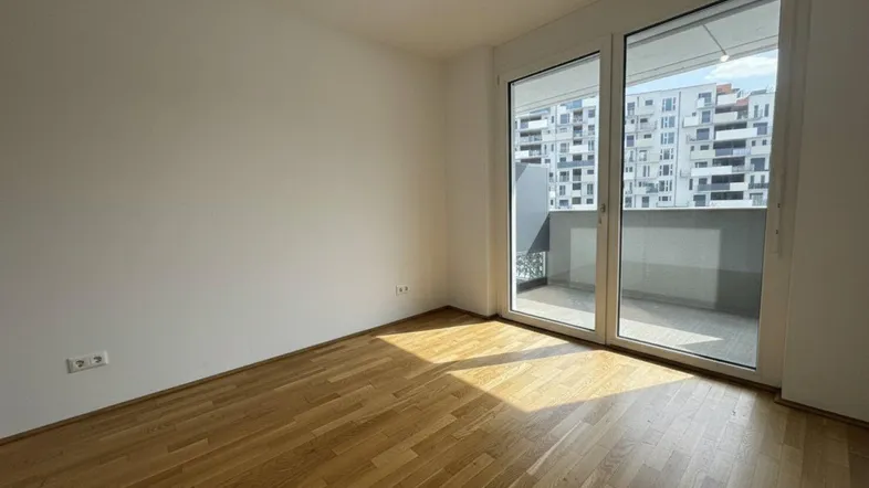Heller Raum mit Holzboden und großen Schiebetüren, die zu einem Balkon führen.