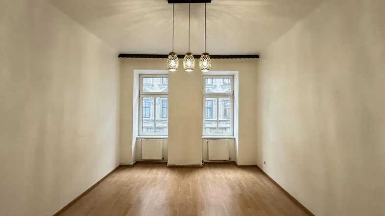 Heller, leerer Raum mit Parkettboden und zwei Fenstern, bereit zur individuellen Gestaltung.