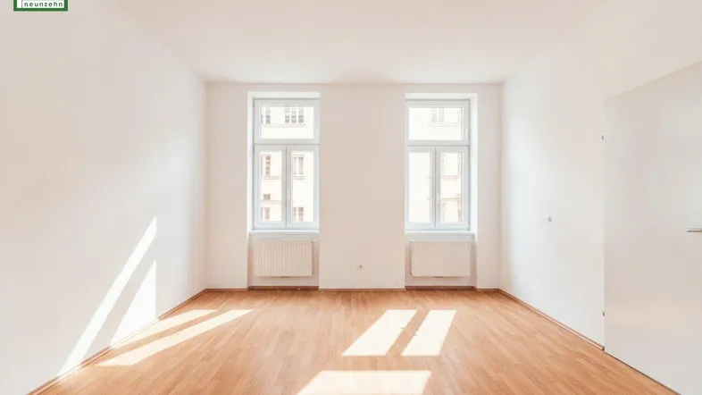 Helles, leeres Zimmer mit Parkettboden und zwei Fenstern, das viel Tageslicht hereinlässt.