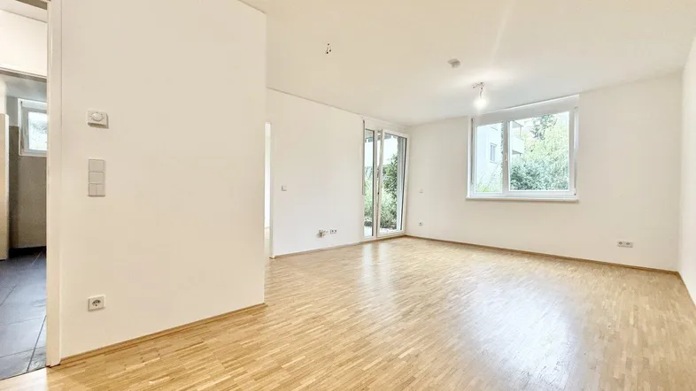 Heller Wohnbereich mit Parkettboden, großen Fenstern und Zugang zu einem Außenbereich.