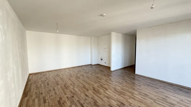 Leeres Zimmer mit hellem Laminatboden und weißen Wänden, bereit zur individuellen Gestaltung.