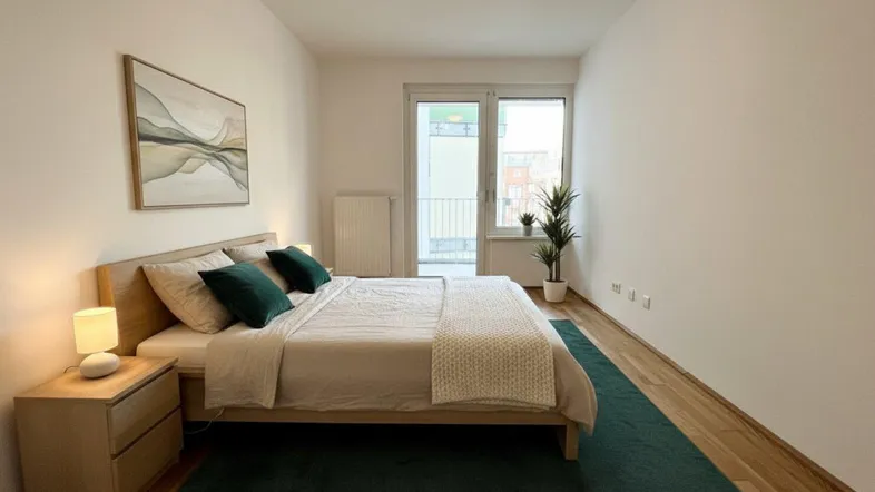 Helles Schlafzimmer mit Holzboden, modernem Bett und direktem Zugang zum Balkon.