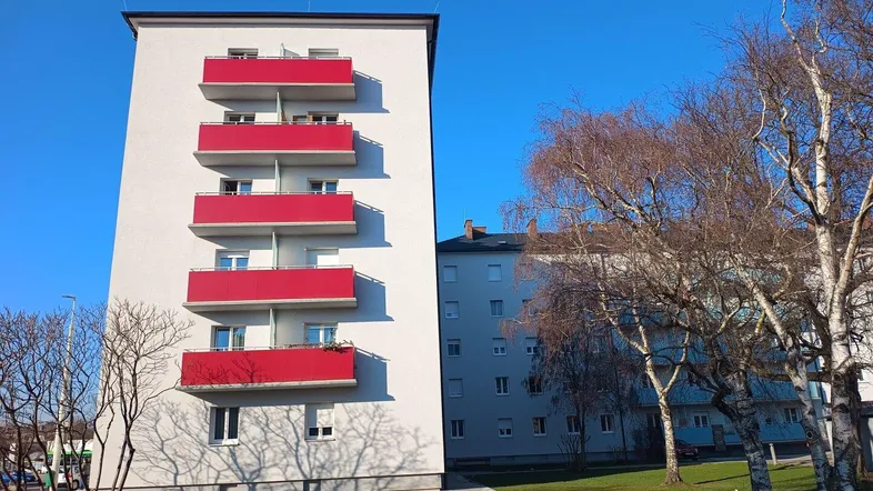 Mehrstöckiges Wohngebäude mit weißer Fassade und roten Balkonen unter blauem Himmel.