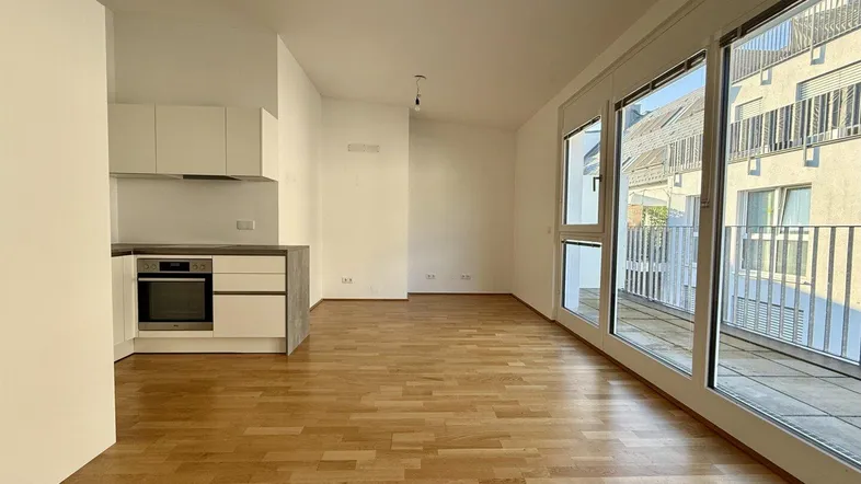 Heller offener Wohn- und Essbereich mit integrierter Küche und Zugang zum Balkon.