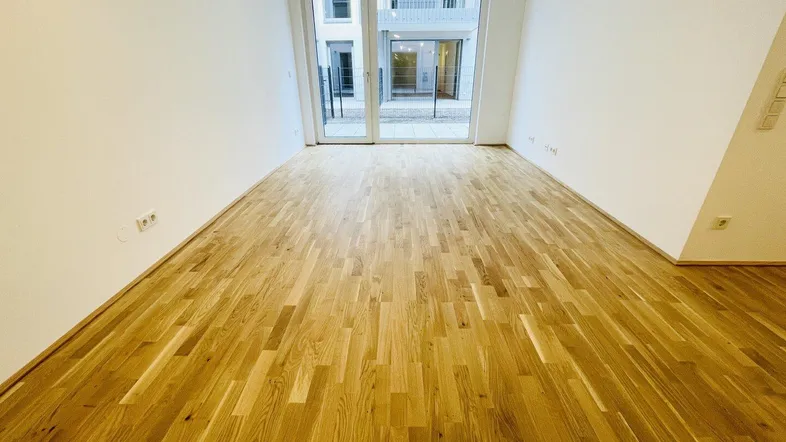Heller Wohnraum mit neuem Parkettboden und Zugang zu einem Außenbereich.