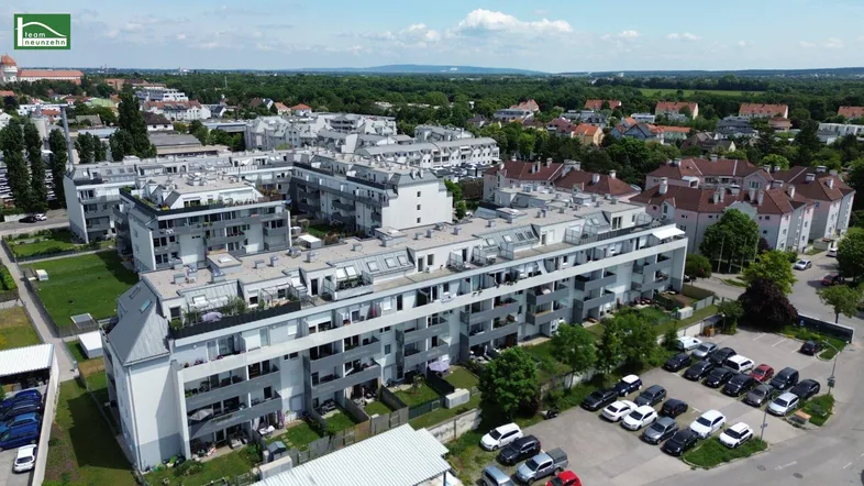 Luftaufnahme einer modernen Wohnanlage mit mehreren Gebäuden und Parkplätzen in einer städtischen Umgebung.