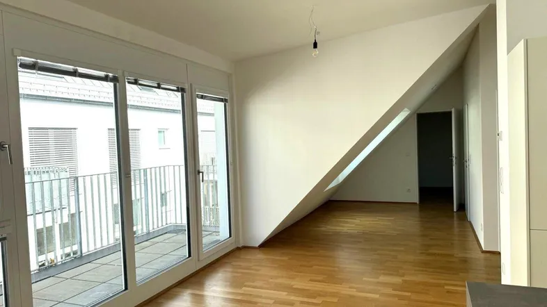 Heller Wohnraum mit Parkettboden, großen Fenstern und Zugang zu einem Balkon im Dachgeschoss.