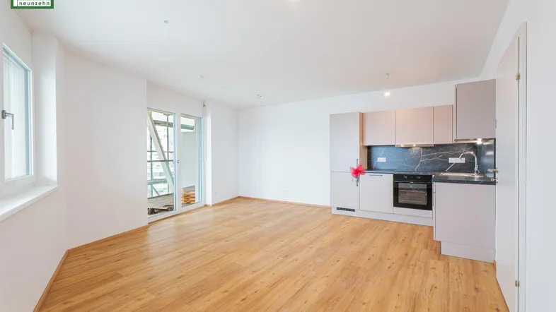 Heller offener Wohnbereich mit integrierter Küchenzeile, Parkettboden und Zugang zum Balkon.