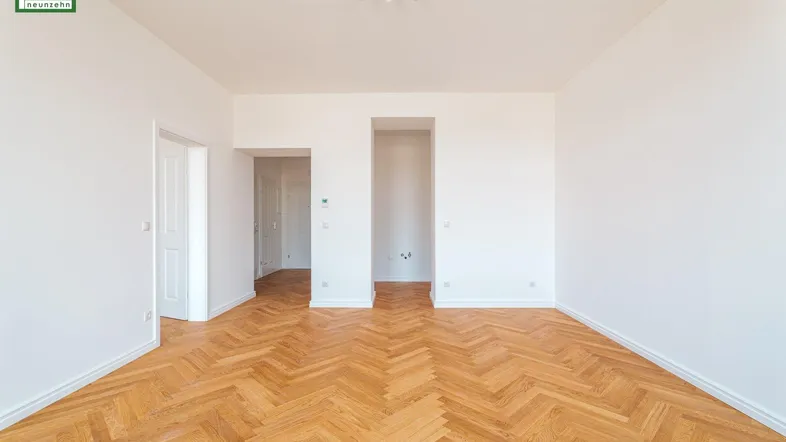 Helles, leeres Zimmer mit Fischgrätparkett und weißen Wänden, bereit zur individuellen Gestaltung.