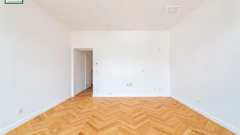 Helles, leeres Zimmer mit Fischgrätparkett und weißen Wänden, bereit zur individuellen Gestaltung.