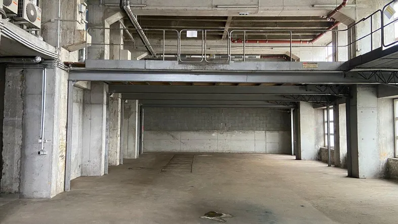 Geräumiger Industriebereich mit hohen Decken, Betonpfeilern und einer Zwischenebene.