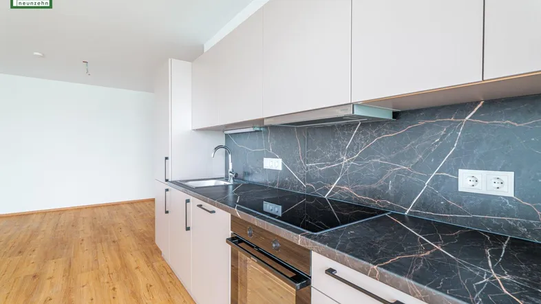 Moderne Einbauküche mit hellen Schränken, dunkler Marmorarbeitsplatte und Holzboden.