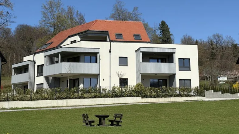 Modernes Mehrfamilienhaus mit Balkonen und Satteldach in grüner Umgebung.