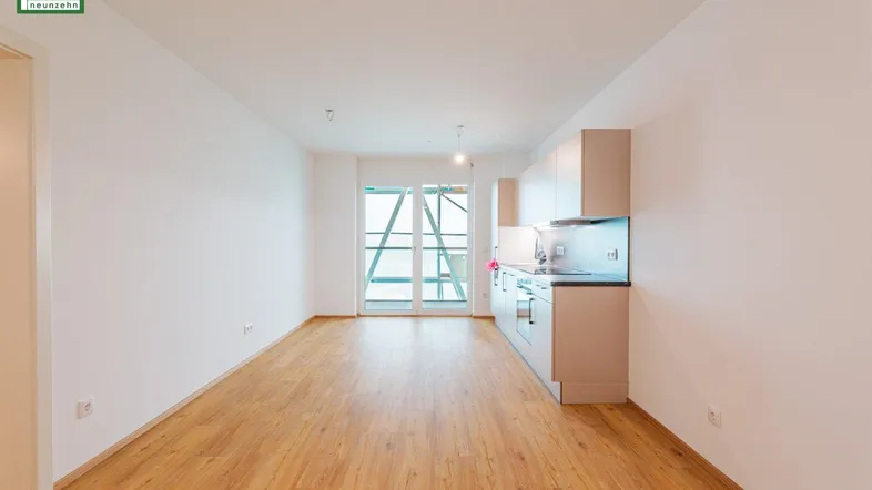 Heller offener Wohnbereich mit integrierter Küche, Laminatboden und Zugang zum Balkon.